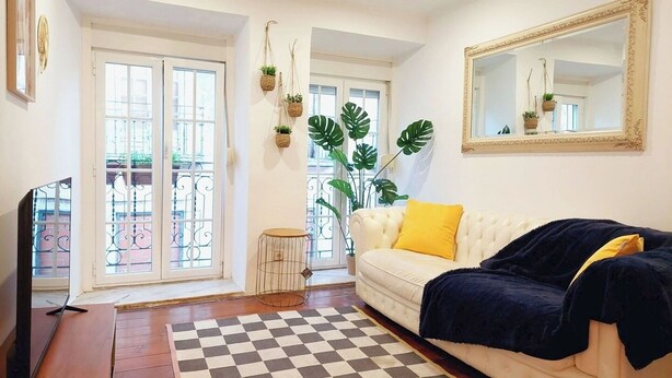 A living room with a checkered rug, a white sofa with a yellow pillow, a large mirror, and a plant.
