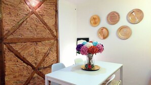 A dining area with a white table, chairs, a vase of colorful flowers, and a brick wall with wooden beams.