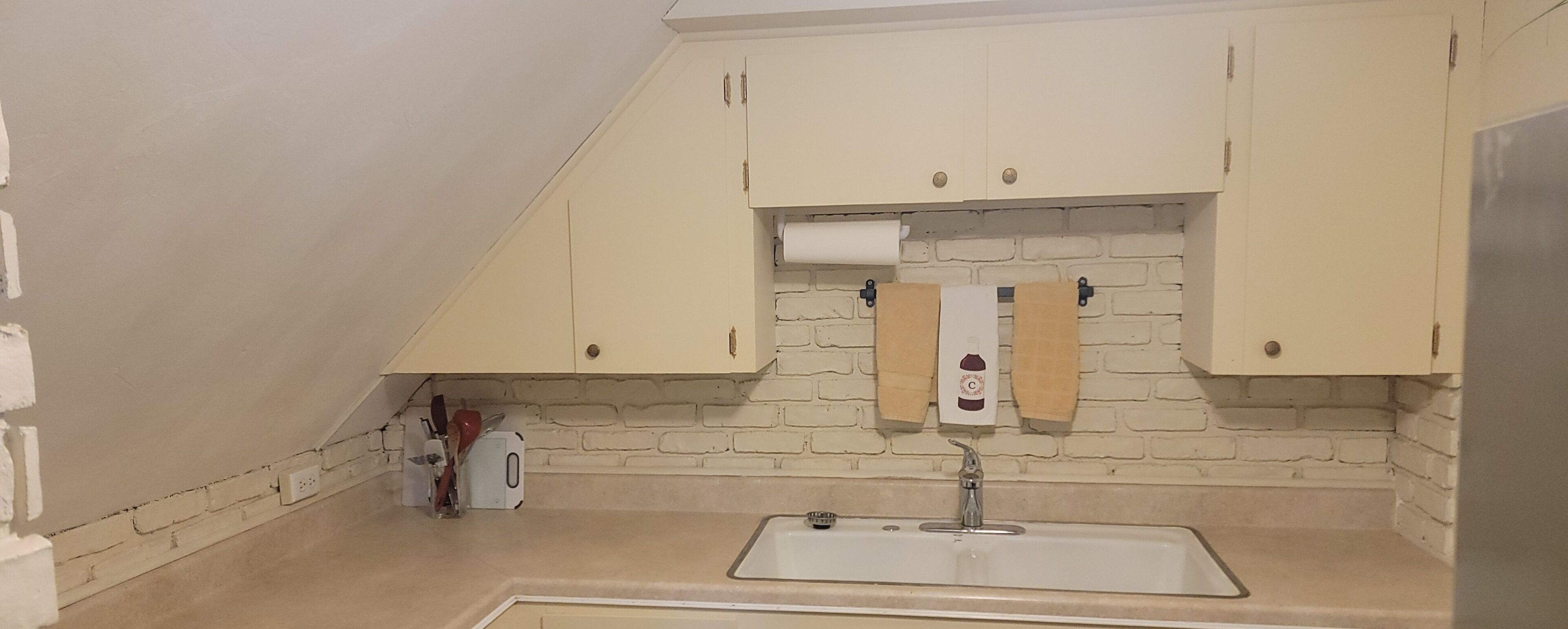 A small kitchen with a sink, a window with a brick wall, and a towel hanging on the wall.