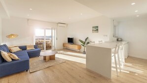 A modern living room with a blue sofa, a wooden coffee table, and a dining area with white chairs. - Baleal Blue Sky - Ocean View (Peniche)