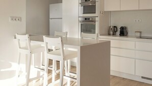 A modern kitchen with white cabinetry, a central island, and a dining area with white chairs. - Baleal Blue Sky - Ocean View (Peniche)