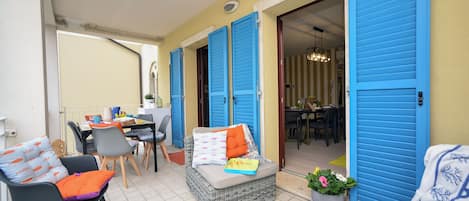 A cozy outdoor seating area with wicker furniture, blue shutters, and a dining table.