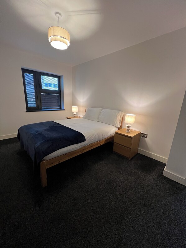 A bedroom with a bed, bedside tables, a window with blinds, and a ceiling light.