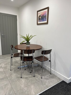 A dining area with a round table, four chairs, a potted plant, and a framed picture on the wall.