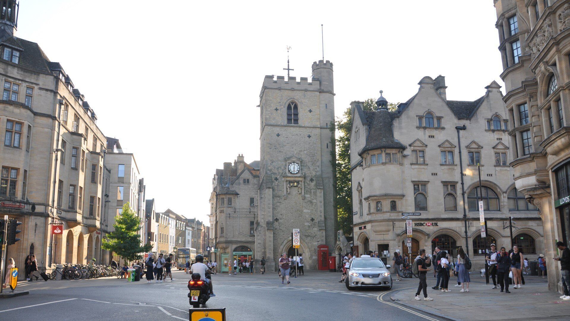Un bâtiment historique doté d’une tour horlogée, une rue pavée et des piétons.