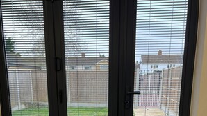 Una habitación con piso alfombrado, un felpudo negro en la entrada y vista a un área exterior con patio y cerca de madera.