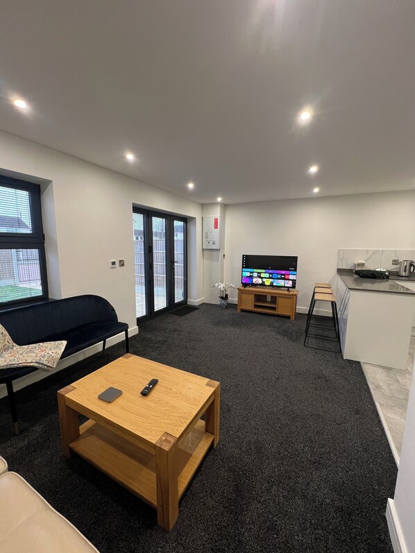 A modern living room with a sofa, a coffee table, a TV, and a kitchen area.