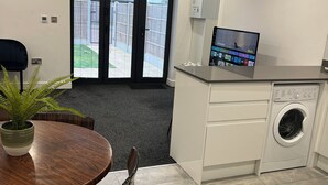 Una cocina moderna con lavadora y secadora integradas, un comedor con mesa redonda y sillas, y un amplio ventanal con vistas a un patio cercado.