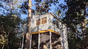 A rustic cabin with a wooden exterior, a porch, and a small deck area surrounded by trees.