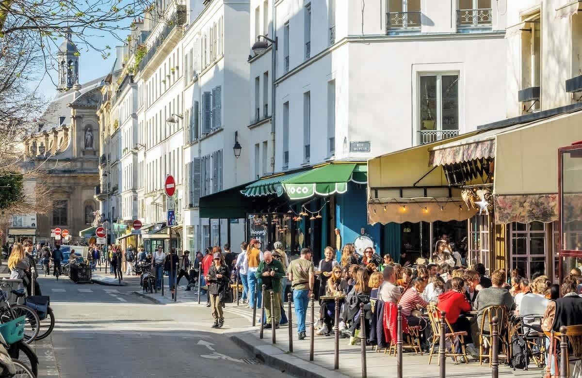 Une rue animée, avec des terrasses de cafés, des piétons et de magnifiques bâtiments d’architecture européenne typique.