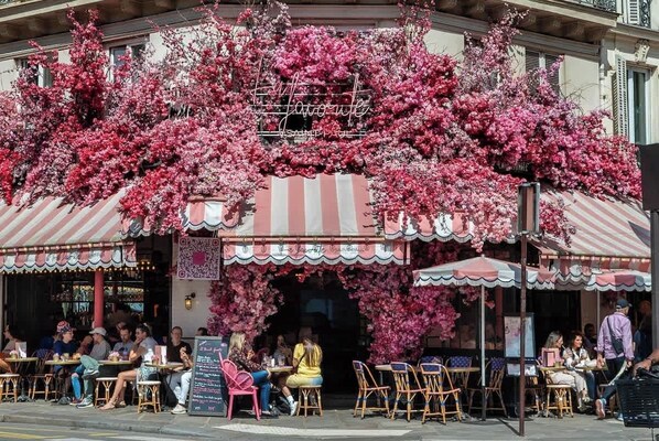 An outdoor café with tables and chairs, a striped awning, and a floral archway.