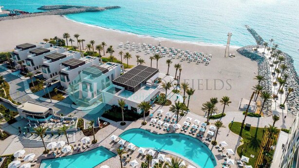 A resort with multiple buildings, a large pool, and a beach area with umbrellas and lounge chairs. - Bloomfields 2BR Plus Maid Fujairah (Al Aqah)
