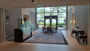 A spacious lobby with a large window offering a view of palm trees and the sea. - Bloomfields 2BR Plus Maid Fujairah (Al Aqah)