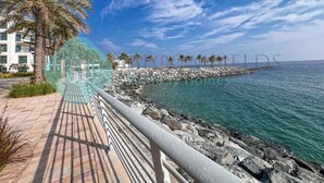 A coastal walkway with palm trees, a rocky shoreline, and a clear blue sky. - Bloomfields 2BR Plus Maid Fujairah (Al Aqah)