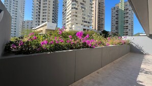 Un immeuble résidentiel moderne doté d’un balcon orné de fleurs roses éclatantes et offrant une vue sur les grands bâtiments environnants.