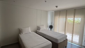 Une chambre avec deux lits simples, un ventilateur de plafond et une grande porte-fenêtre coulissante donnant sur un espace extérieur.