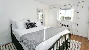 A modern bedroom with a bed, a window with curtains, a radiator, and a mirror. - The Gathering Place | Ocean Views | Hot Tub | Pickleball (Grayland)