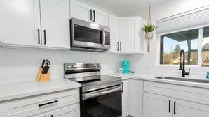A modern kitchen with white cabinets, stainless steel appliances, and a window with a view. - The Gathering Place | Ocean Views | Hot Tub | Pickleball (Grayland)