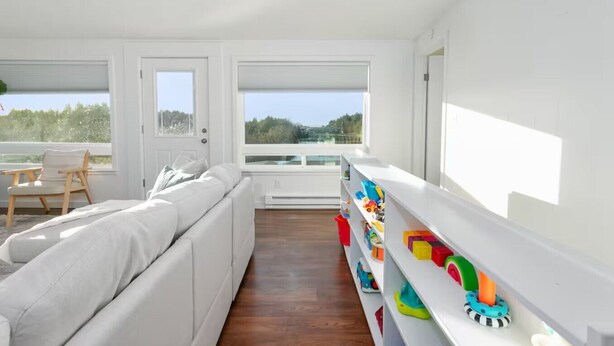 A bright, white room with a sofa, a chair, and a window overlooking greenery. - The Gathering Place | Ocean Views | Hot Tub | Pickleball (Grayland)