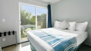 A bedroom with a bed, a sliding glass door to the outside, and a small table by the door. - Nautical Queen Bedroom, Pickleball (Grayland)