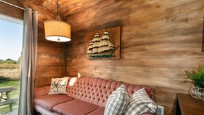 Una stanza accogliente con parete in legno, un divano trapuntato, una lampada a sospensione e un'opera d'arte a tema nautico.