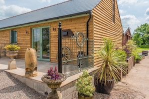 Un bâtiment en bois avec une porte verte, un portail en métal et diverses plantes en pot.