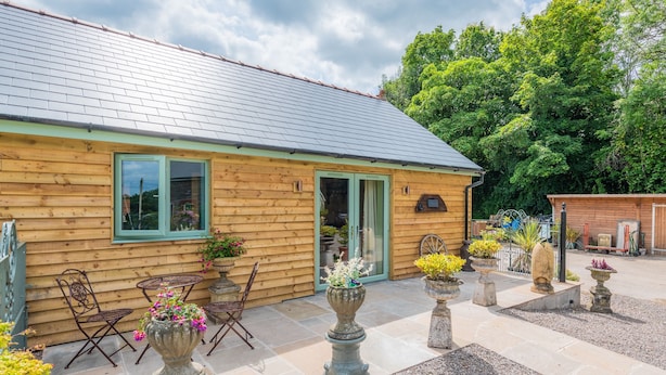 A wooden cabin with a tiled patio, outdoor seating, and potted plants. - Garden View Barn, 1-bed, Sleeps 4 With Parking (Cowbridge)