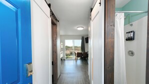 Un couloir avec une porte bleue, une porte en bois et un espace douche séparé par un rideau.