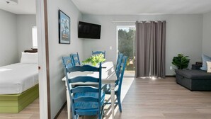 A modern room with a bed, a dining table with chairs, a TV mounted on the wall, and a sofa.