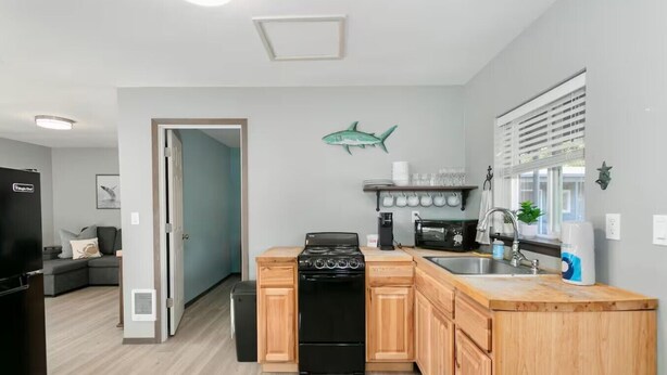 A compact kitchen with a stove, microwave, and sink, wooden cabinets, and a teal shark decoration on the wall.