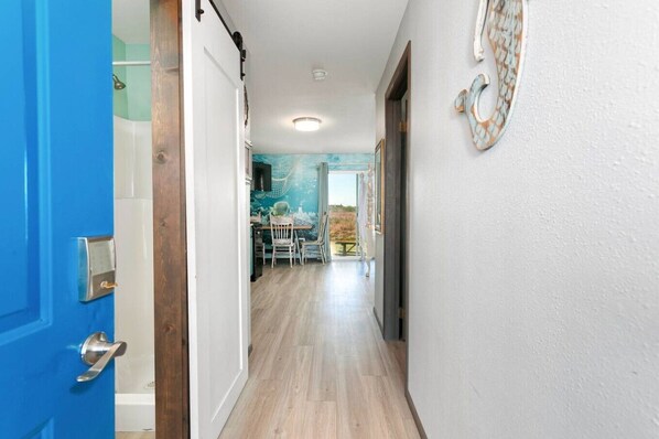 A hallway with a blue door, a dining area with a table and chairs, and a view of the outdoors.