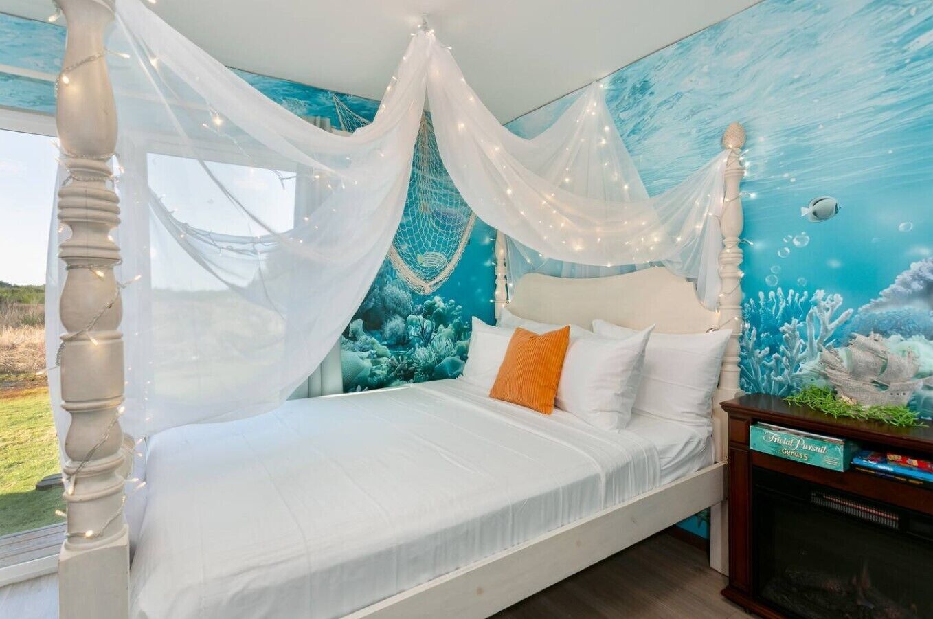 Une chambre à coucher avec un lit, un baldaquin blanc et une fresque représentant un paysage sous-marin.