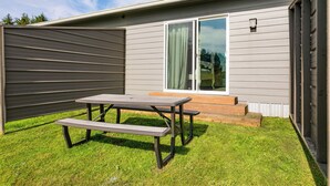 A patio with a picnic table and benches, a sliding glass door, and a small step leading to a covered area.