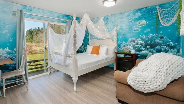 A bedroom with a four-poster bed, a view of the outdoors, and a mural of an underwater scene.
