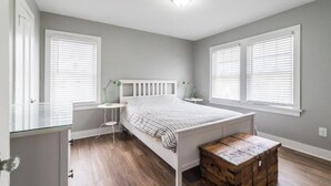 Quarto com cama, mesas de cabeceira, cômoda e janela com persianas.