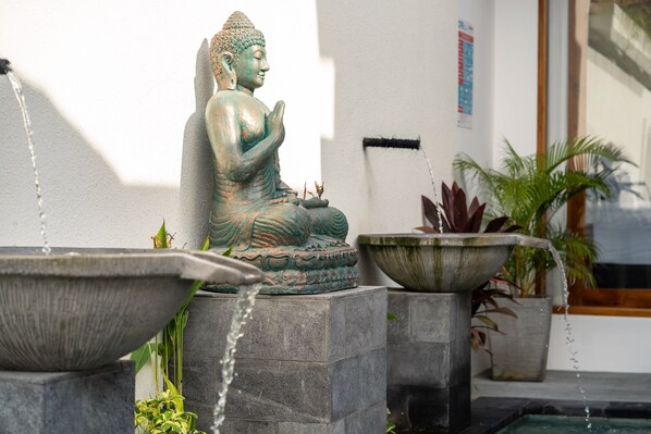 Una estatua de Buda en posición sentada, con agua que fluye de dos cuencas delante.