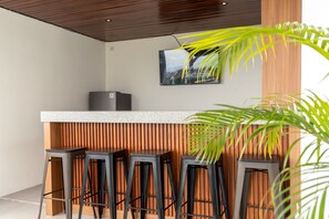 A modern bar area with a wooden slatted wall, a granite countertop, and four black bar stools. - 4BR Villa Uluwatu | Pool | 7 min to Melasti Beach | Rooftop Bar | Sunset Views | (Bali)