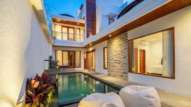 Ein moderner Poolbereich im Freien mit einer Steinwand und einer Holzterrasse, umgeben von weißen Wänden und großen Fenstern.