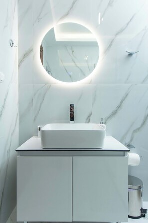 Bathroom features a large mirror, sink, and lighting above a white cabinet.