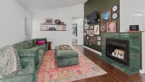Una sala de estar con un sofá verde, un reposapiés a juego, un tapete estampado, una chimenea y varias imágenes enmarcadas en las paredes.