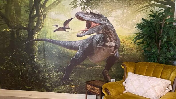 A room with a mural of a dinosaur, a yellow velvet armchair, and a small wooden side table. - Dino Den - Charming 1-bedroom apartment in Oneonta with WiFi, AC (Oneonta)