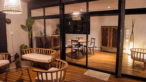 Una terraza de madera con un ventanal de vidrio que da a un comedor con mesa y sillas.