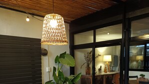 Una zona de estar acogedora con muebles de madera, una planta grande en maceta y una lámpara colgante.