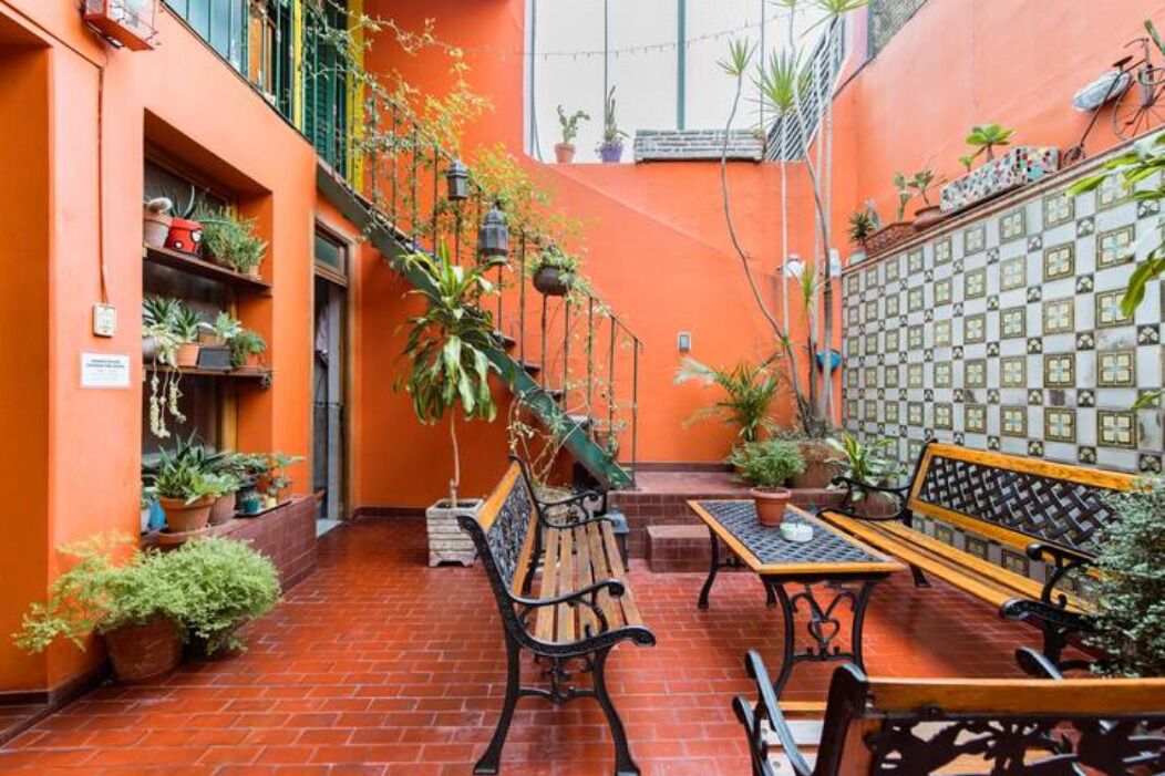Um pátio com piso de tijolos, um banco de madeira, uma mesa e plantas em vasos.