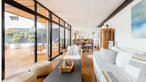Un salón moderno con un amplio ventanal, suelo de madera y sofá blanco.