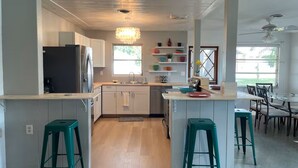 A modern kitchen with a central island, two green bar stools, and a dining area with a table and chairs. - Waterfront Family Retreat, heated pool, 2 miles from the Beach (Englewood)