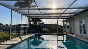 A swimming pool with a glass enclosure, surrounded by a grassy area and palm trees. - Waterfront Family Retreat, heated pool, 2 miles from the Beach (Englewood)
