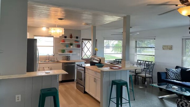 A modern kitchen with a central island, bar stools, and a dining area with a glass table and chairs. - Waterfront Family Retreat, heated pool, 2 miles from the Beach (Englewood)