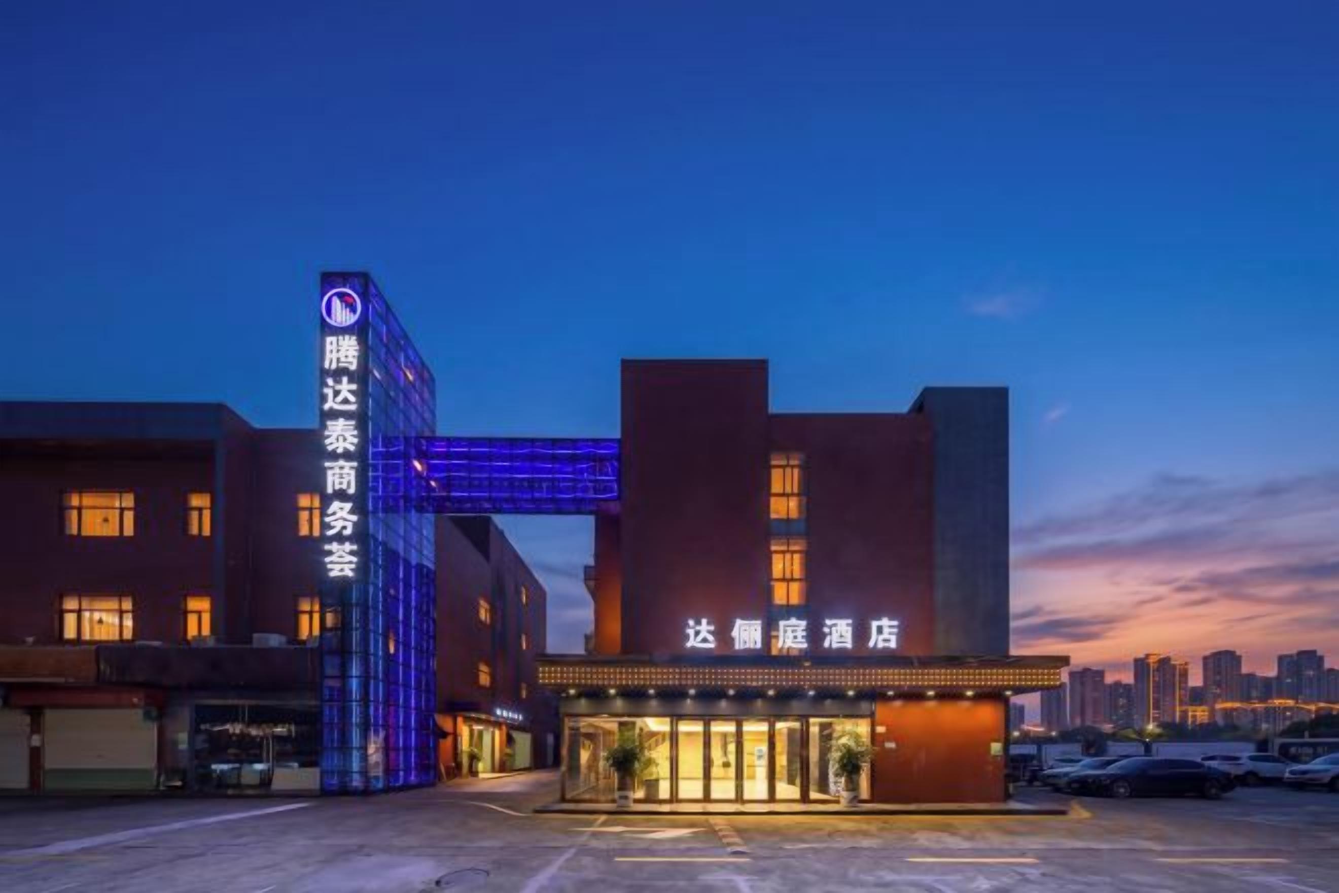 A hotel with a prominent entrance and signage, a parking area, and a city skyline in the background.