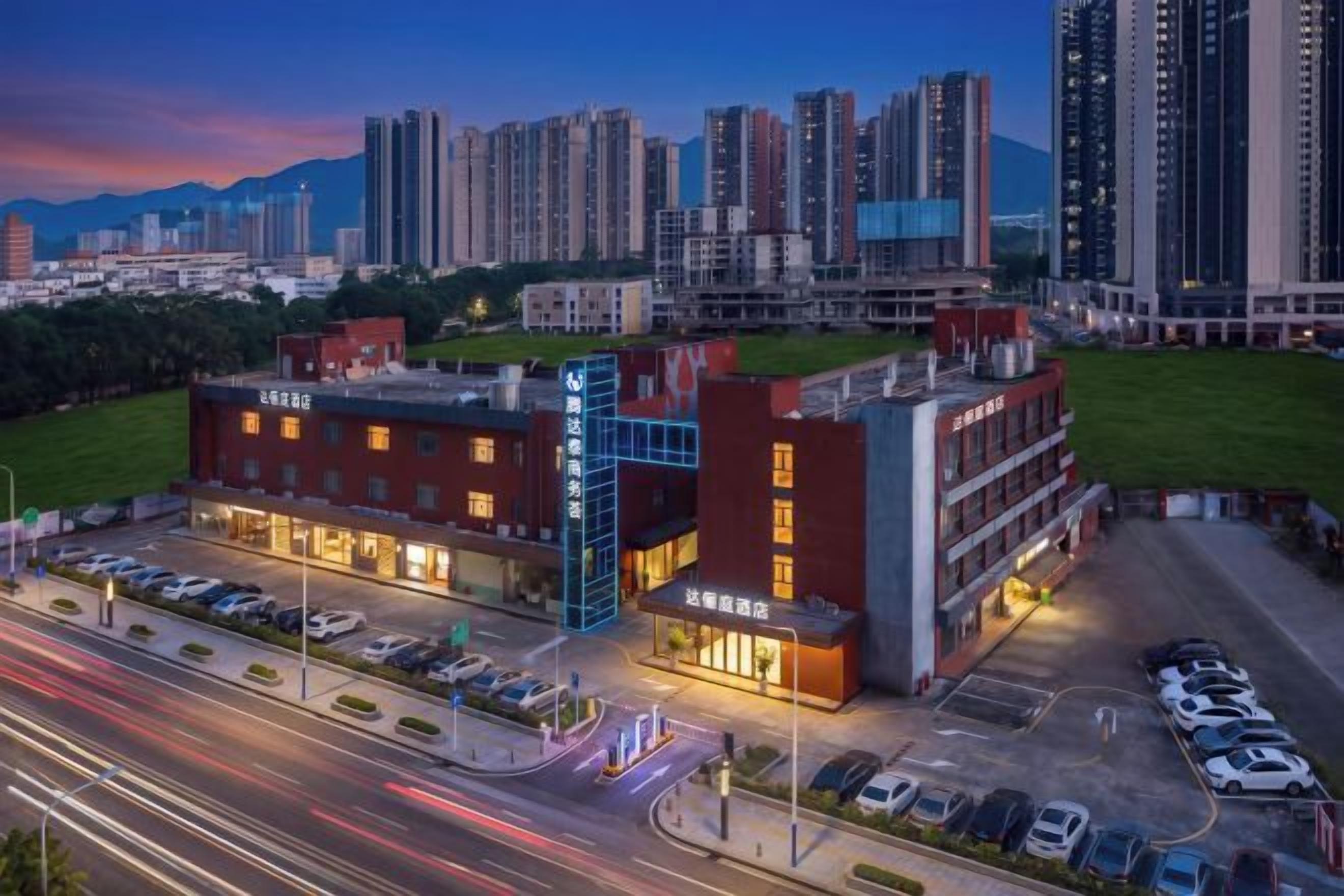 A multi-story hotel with a parking lot in front, surrounded by high-rise buildings.